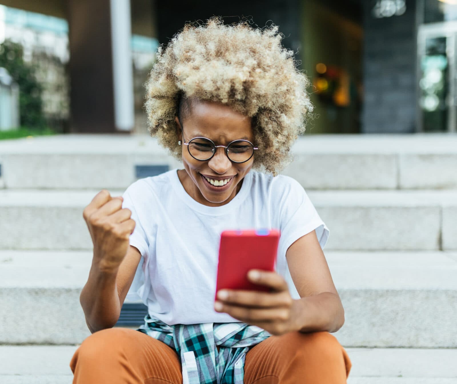 Happy afro woman celebrating victory while receiving good news on her mobile phone. Technology and ...